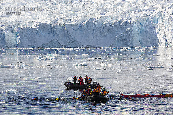 Mitglieder einer Expeditionskreuzfahrt in die Antarktis beim Seekajakfahren und Schwimmen in der Paradise Bay unterhalb des Mount Walker auf der antarktischen Halbinsel. Die antarktische Halbinsel ist eines der sich am schnellsten erwärmenden Gebiete der Erde.