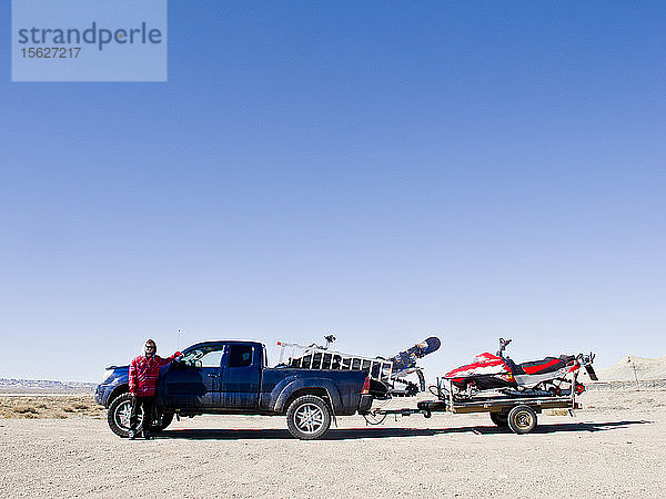 Ein Mann steht neben seinem mit zwei Motorschlitten beladenen Pickup mitten in der Wüste von Utah.