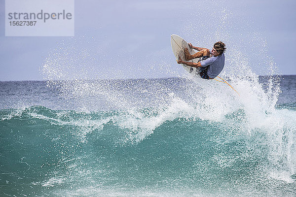Ein männlicher Surfer holt Luft und hält sich an der Kante seines Brettes an der Nordküste von Oahu  Hawaii  fest.