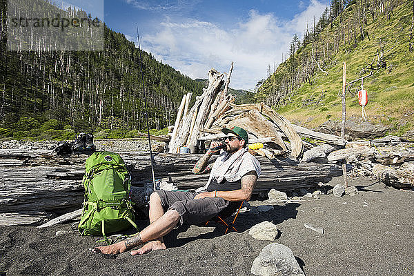 Ein Mann entspannt sich mit Flachmann und Zigarre auf seinem Zeltplatz an der Lost Coast