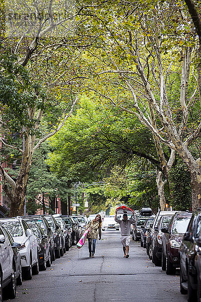 Paar mit Paddelbrettern in der Mitte der Straße zwischen Reihen geparkter Autos  New York City  New York  USA