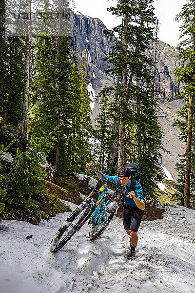 Mountainbikerin in malerischer Landschaft schiebt ihr Fahrrad durch den Schnee auf dem Ice Lakes Trail  USA