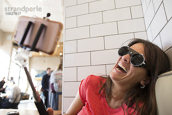 Lachende Frau  die in einem Café ein Selfie mit einem Selfie-Stick macht  Santa Cruz  Kalifornien  USA