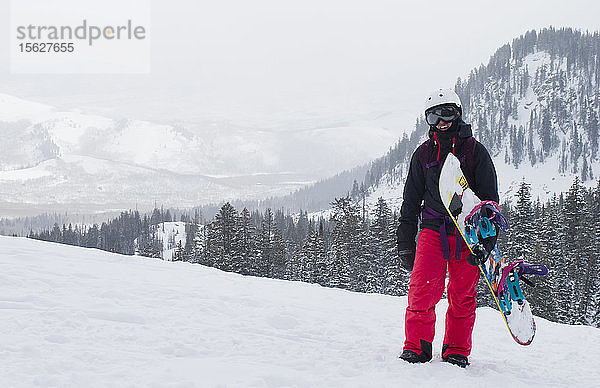 Ein Mädchen steht auf und macht eine kurze Pause nach einer Wanderung mit ihrem Snowboard im Hinterland von Utah.