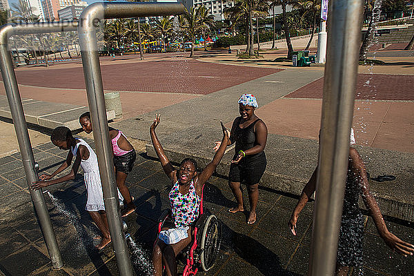 Mädchen  darunter eines im Rollstuhl  lachen  spielen und duschen  nachdem sie im öffentlichen Schwimmbad auf der Promenade der Goldenen Meile in Durban  Südafrika  waren