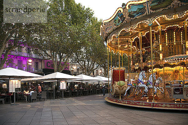 Während Spaziergänger in den Cafés das abendliche Angebot erkunden  sorgt das Karussell auf dem Place de L'Horloge in Avignon  Frankreich  für Spaß.