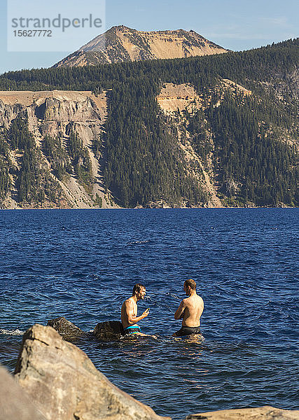 Blick auf zwei junge Männer  die hüfttief im Crater Lake stehen  mit Bergen im Hintergrund  Oregon  USA