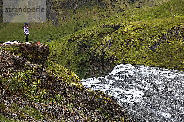 Touristen besuchen den Skogafoss  einen der berühmtesten Wasserfälle in Island. Der Wasserfall liegt in der Nähe des Highway One (auch bekannt als Ringstraße) und stürzt 60 Meter in die Tiefe  und es gibt Wege  die es den Besuchern ermöglichen  bis zum unteren und oberen Ende des Wasserfalls zu gehen. Der Wasserfall liegt am Fluss Skoga  der durch das isländische Hochland fließt  bevor er den Atlantik erreicht.ï¾