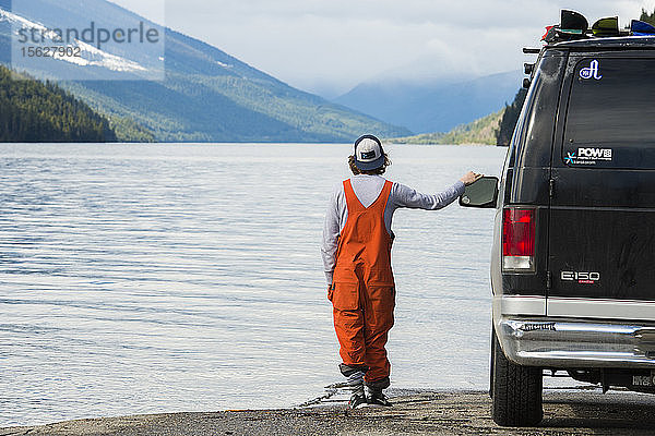 Snowboarder stehend neben seinem Van am Rande eines Sees mit Blick auf die Landschaft
