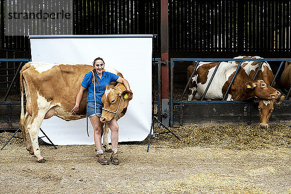 Porträt einer Bäuerin  die mit einer Guernsey-Kuh vor einem Stall steht.