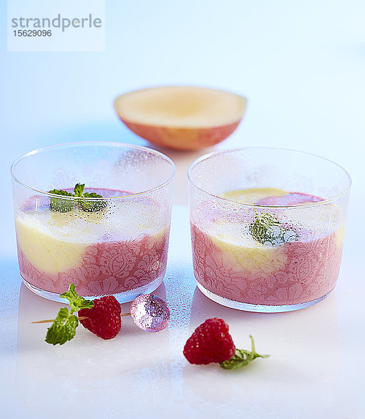Himbeer-Mango-Smoothie in zwei kleinen Gläsern mit Joghurt  Milch  Melisse