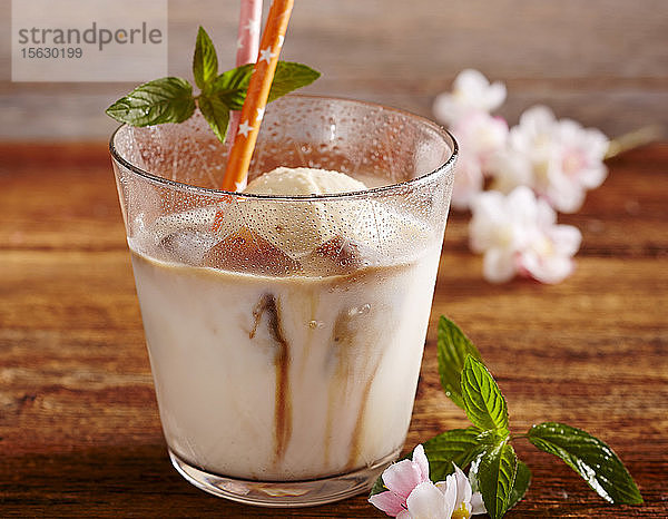 Mandelmilch mit Vanilleeis und Kaffee-Eiswürfeln im Glas mit Trinkhalm und Minze