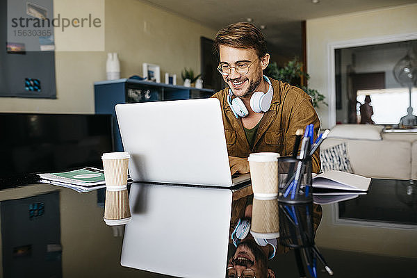 Lächelnder Mann arbeitet zu Hause am Tisch mit einem Laptop