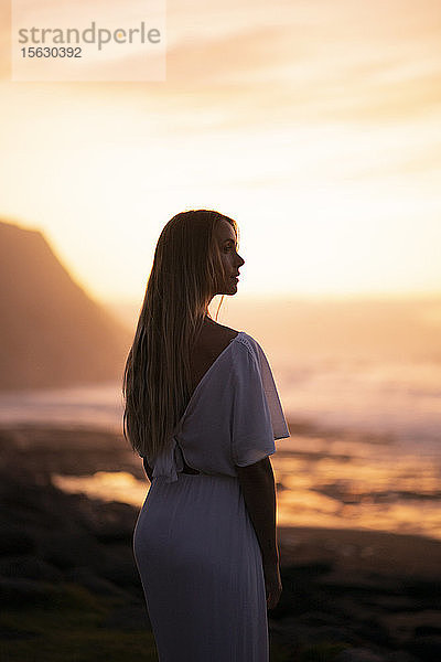 Junge Frau am Strand bei Sonnenaufgang mit seitlichem Blick