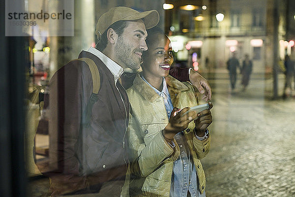 Junges Paar mit Smartphone beobachtet nachts etwas in der Stadt  Lissabon  Portugal