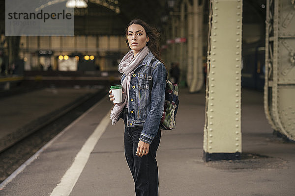 Junge weibliche Reisende mit Kaffee zum Mitnehmen auf den Bahnsteig