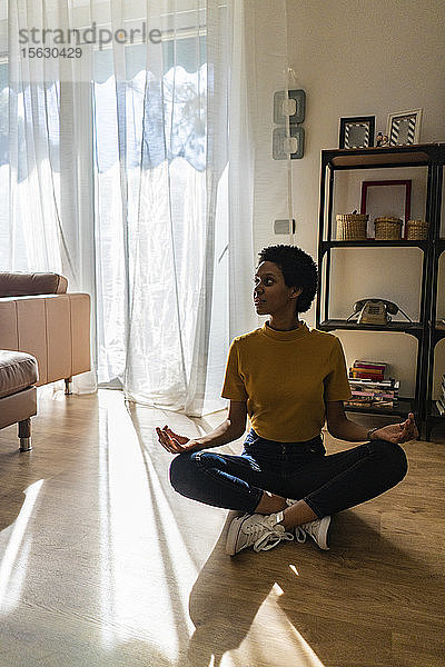 Junge Frau  die zu Hause in Yoga-Pose auf dem Boden sitzt