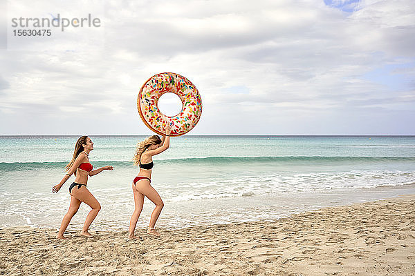 Zwei junge Frauen mit einem großen aufblasbaren Ring am Strand
