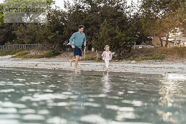 Glücklicher Vater rennt mit Tochter am Meeresufer