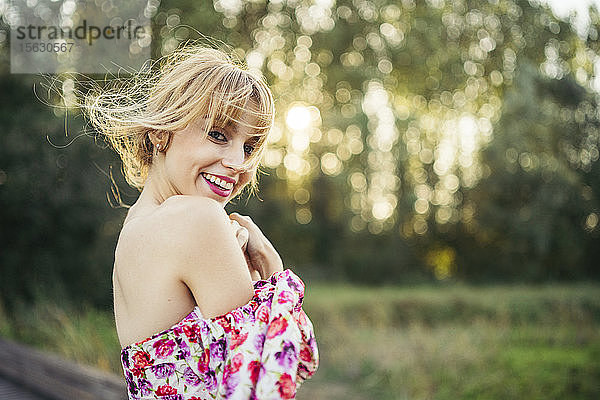 Porträt einer glücklichen jungen Frau in Sommerkleid mit Blumenmuster in Natur
