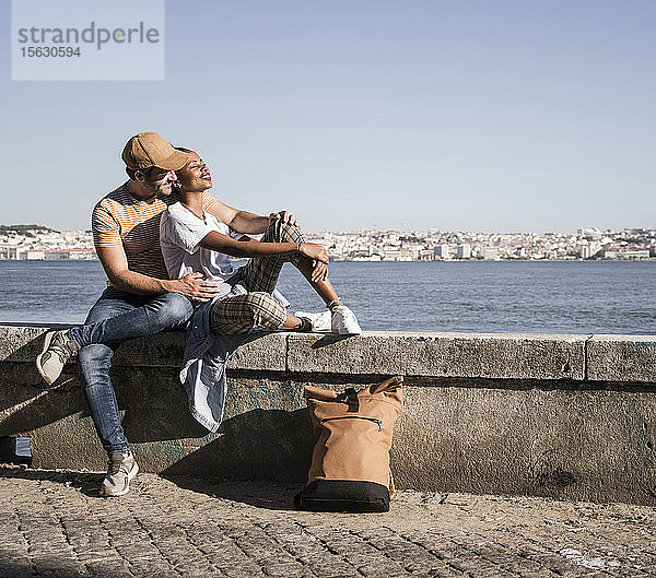 Junges Paar sitzt auf einer Mauer am Wasser  Lissabon  Portugal