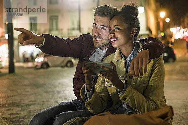 Porträt eines jungen Paares mit Smartphone  das nachts etwas in der Stadt beobachtet  Lissabon  Portugal