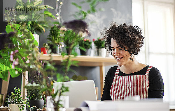 Lächelnde junge Frau mit Laptop in einem kleinen Laden mit Pflanzen