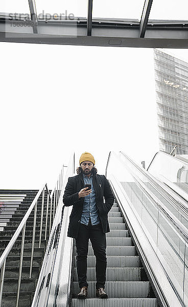 Mann steht auf Rolltreppe und schaut auf Smartphone  Berlin  Deutschland