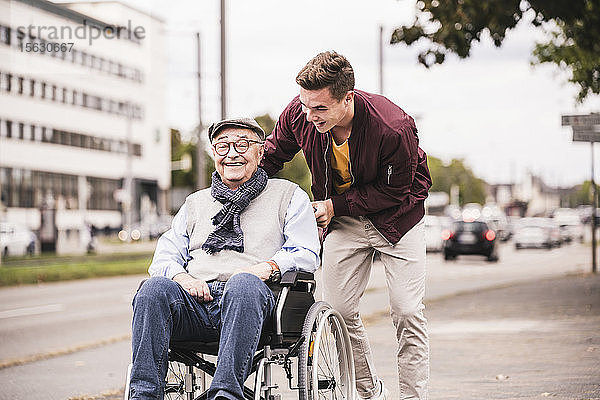 Junger Mann schiebt glücklichen älteren Mann im Rollstuhl