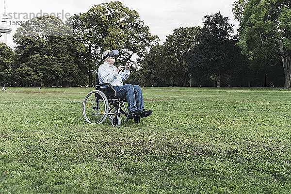Älterer Mann sitzt im Rollstuhl in einem Park und benutzt eine Virtual-Reality-Brille