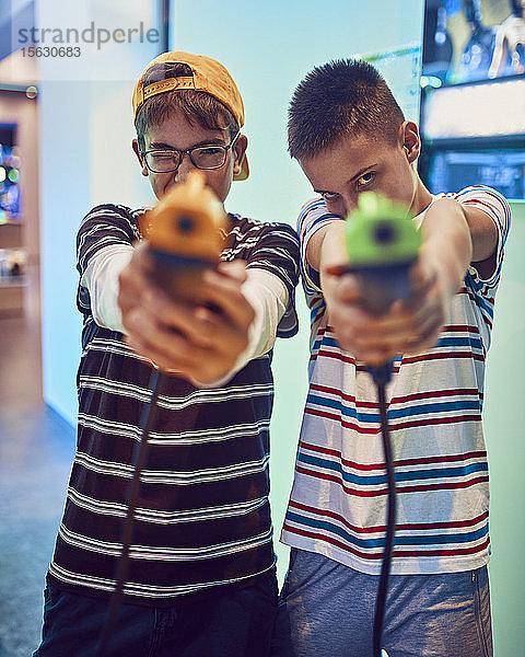 Porträt von jugendlichen Freunden  die in einer Spielhalle mit Pistolen schießen