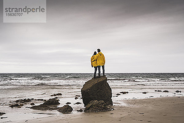 Junge Frau in gelben Regenjacken und auf einem Felsen am Strand stehend  Bretagne  Frankreich