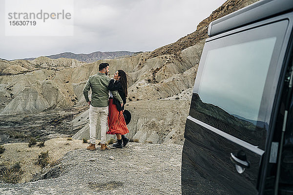 Junges Paar in Wüstenlandschaft unter bewölktem Himmel neben dem Wohnmobil  Almeria  Andalusien  Spanien