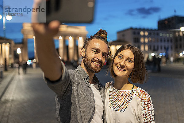 Glückliches Paar beim Selfie am Brandenburger Tor zur blauen Stunde  Berlin  Deutschland