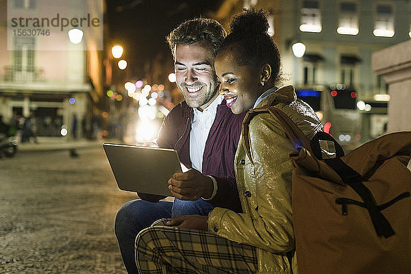Portrait eines glücklichen jungen Paares mit digitalem Tablet in der Stadt bei Nacht  Lissabon  Portugal