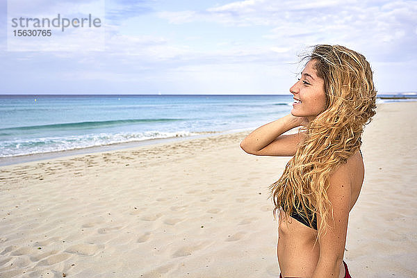 Lächelnde junge Frau steht am Strand