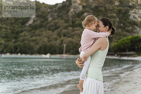 Glückliche Mutter trägt ihre Tochter am Strand