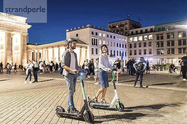 Junges Paar mit Elektrorollern am Brandenburger Tor bei Nacht  Berlin  Deutschland