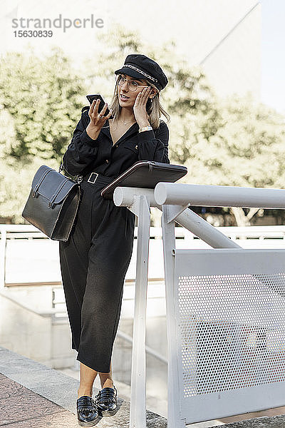 Junge blonde Geschäftsfrau mit schwarzem Hut und Smartphone