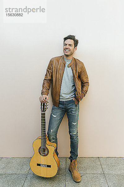 Lächelnder Mann mit Gitarre vor einer Wand