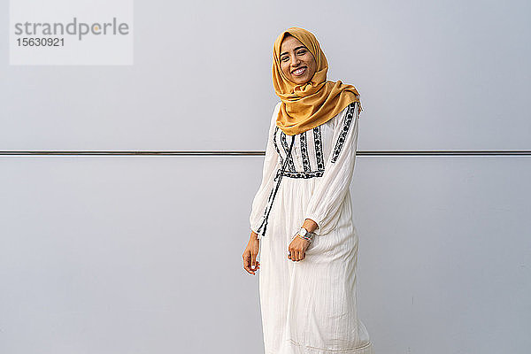 Junge muslimische Frau  die einen gelben Hidschab trägt und vor einer weißen Wand läuft