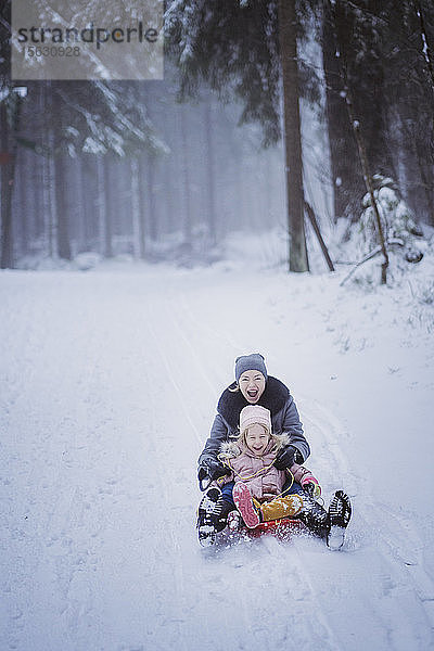 Porträt einer reifen Frau  die zusammen mit ihrer Tochter Schlitten fährt