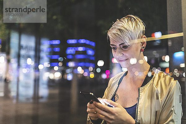 Porträt einer lächelnden blonden Frau  die nachts in der Stadt mit dem Handy telefoniert  Berlin  Deutschland