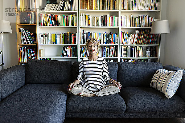 Reife Frau  die zu Hause auf der Couch Yoga praktiziert