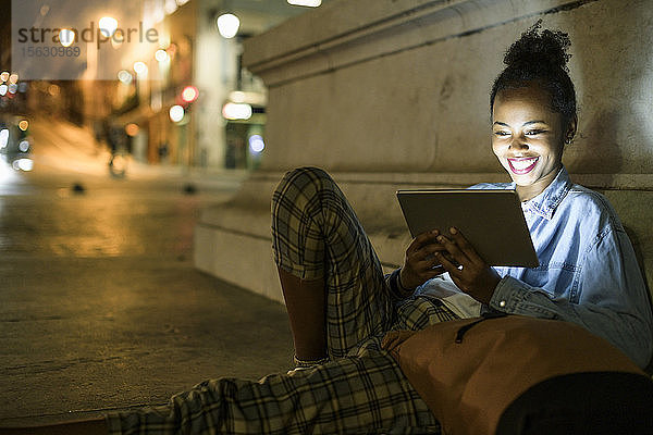 Portrait einer glücklichen jungen Frau mit digitalem Tablet in der Stadt bei Nacht  Lissabon  Portugal