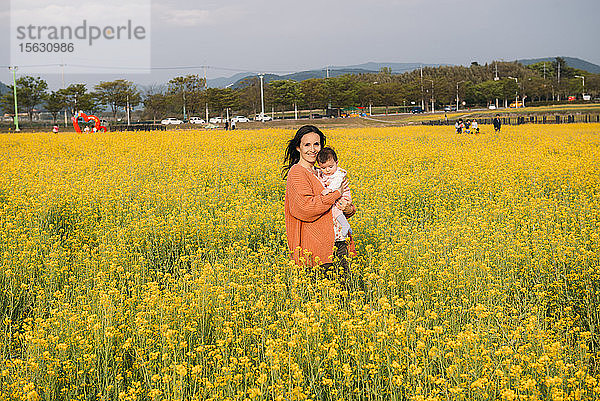 Porträt einer glücklichen Frau mit einem kleinen Mädchen auf dem Arm in einem Vergewaltigungsfeld stehend  Gyeongju  Südkorea