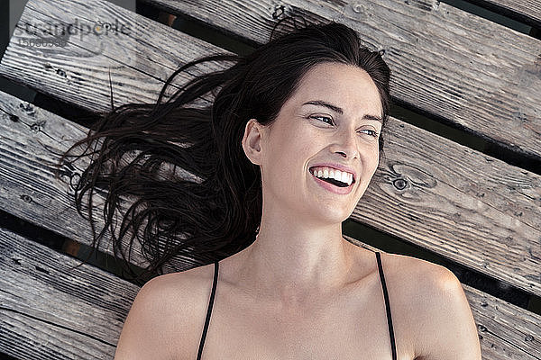 Porträt einer lachenden jungen Frau  die sich auf einem Steg entspannt