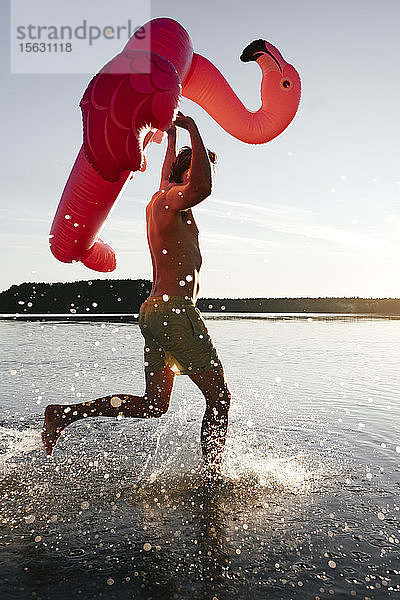 Junger Mann rennt mit Flamingo-Pool in einen See
