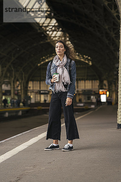 Junge weibliche Reisende steht mit Kaffee auf dem Bahnsteig