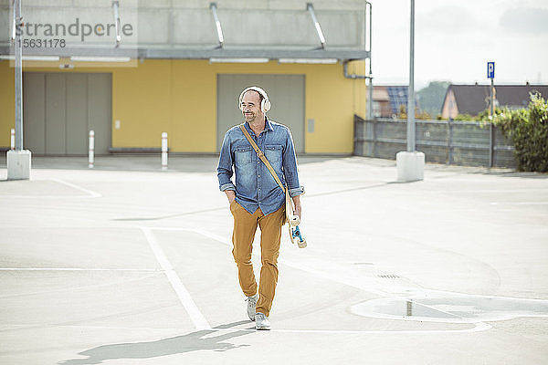 Lässiger reifer Mann mit Kopfhörern und Skateboard auf dem Parkdeck